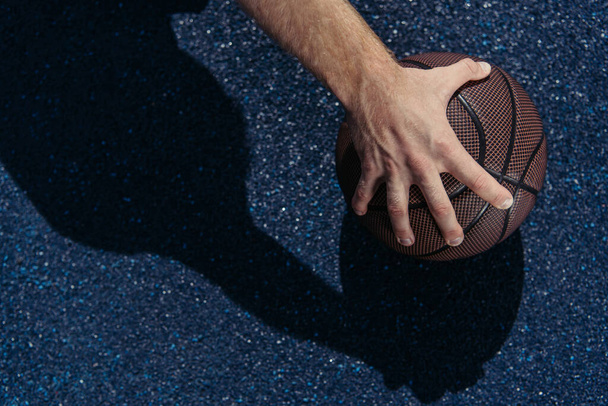 cropped view of sportsman holding ball near asphalt - Fotó, kép