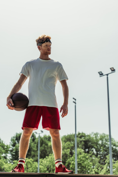 full length of man in white t-shirt and red shorts standing with ball outdoors - Photo, image