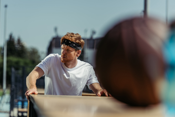 redhead sportsman in bandana looking away near blurred ball - Fotó, kép