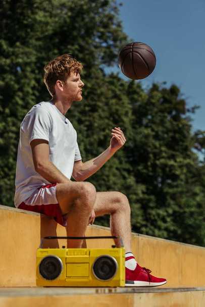 redhead man playing with ball while sitting near boombox - Photo, Image