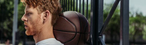 πλαϊνή άποψη του παίκτη μπάσκετ με μπάλα κοντά φράχτη, πανό - Φωτογραφία, εικόνα