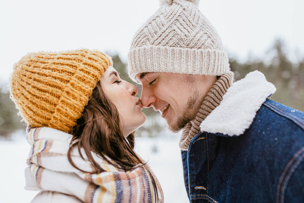people, love and leisure concept - happy woman kissing mans nose in winter forest - 写真・画像