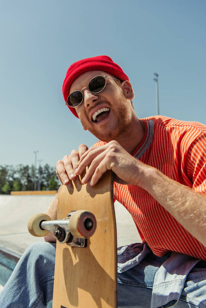 ενθουσιασμένοι άνθρωπος με γυαλιά ηλίου γέλιο κοντά skate σε εξωτερικούς χώρους - Φωτογραφία, εικόνα