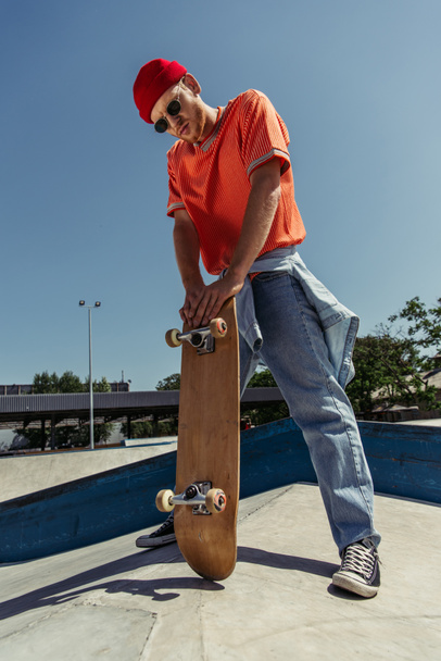 full length of trendy skater standing with skateboard outdoors - Foto, Imagem