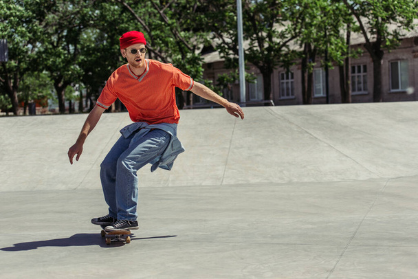 full length of man in orange t-shirt and red beanie riding in skate park - Zdjęcie, obraz