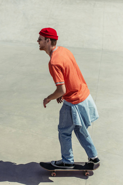 side view of man in orange t-shirt and red beanie riding skateboard - 写真・画像