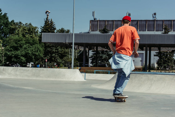 back view of man in orange t-shirt skateboarding in urban skate park - Photo, Image