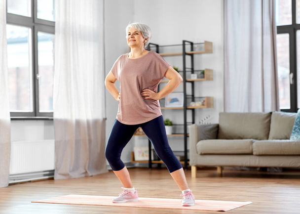 sport, fitness and healthy lifestyle concept - smiling senior woman exercising on mat at home - Foto, afbeelding