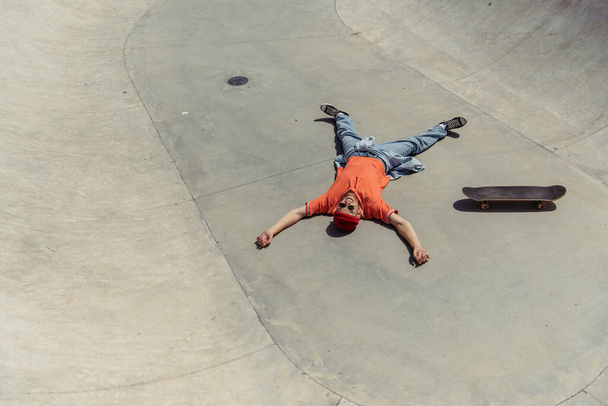 θέα υψηλής γωνίας του χαρούμενου άνδρα χαλάρωση κοντά skateboard στη ράμπα - Φωτογραφία, εικόνα