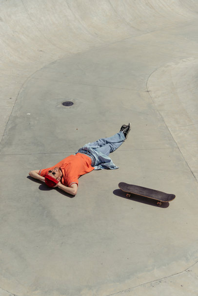 άποψη υψηλής γωνίας της μόδας και χαρούμενος άνθρωπος που βρίσκεται κοντά στο skateboard - Φωτογραφία, εικόνα