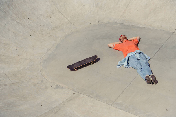 άποψη υψηλής γωνίας του trendy άνθρωπος που βρίσκεται κοντά skateboard στο πάρκο skate - Φωτογραφία, εικόνα