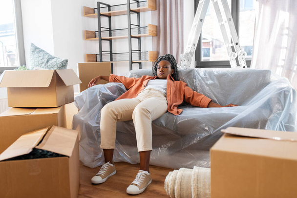 moving, people and real estate concept - tired woman with boxes sleeping on sofa at new home - Valokuva, kuva