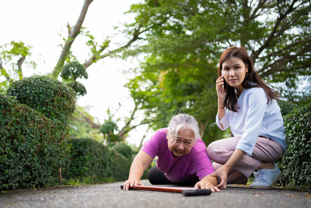 Asian senior woman fell down on lying floor because faint and limb weakness and pain from accident and woman came to help support and call emergency. Concept of old elderly insurance and health care - Photo, image