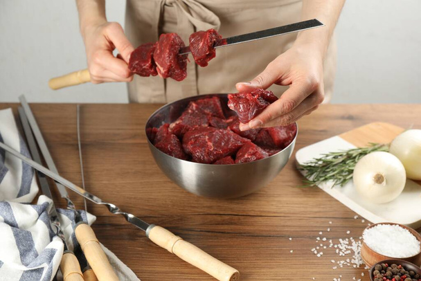 Woman stringing marinated meat on skewer at wooden table, closeup - Foto, Imagen