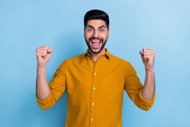 Portrait of positive overjoyed ecstatic person dressed yellow shirt holding hands clenching fists excited sale isolated on blue color background. - Fotografie, Obrázek