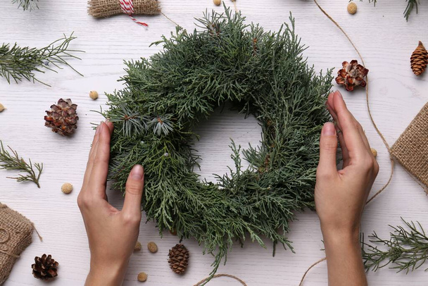 Florist with beautiful Christmas wreath of fir branches at white wooden table, top view - 写真・画像