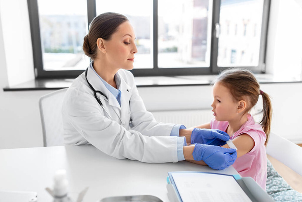 medicine, healthcare and vaccination concept - female doctor or pediatrician attaching medical patch to little girl patients hand at clinic - Foto, Imagem