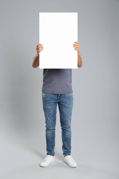 Man holding white blank poster on grey background. Mockup for design - Photo, Image