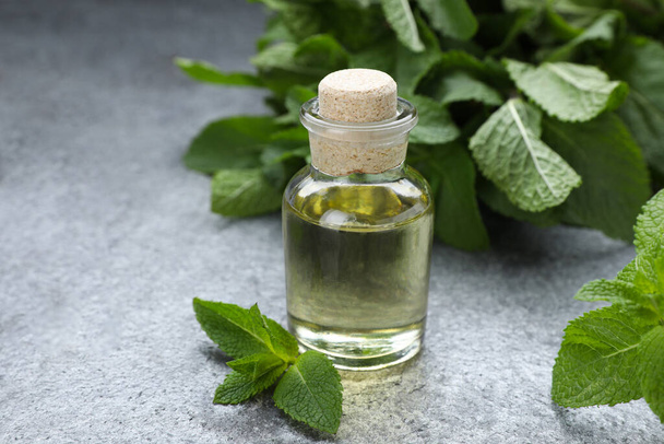 Bottle of essential oil and mint on grey table, closeup - Foto, afbeelding