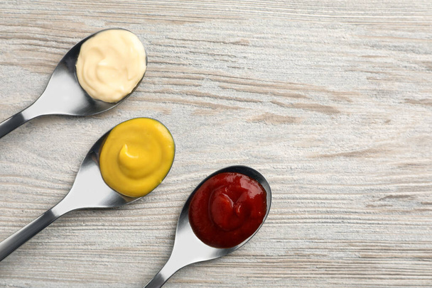 Spoons with mustard, ketchup and mayonnaise on wooden table, flat lay. Space for text - Foto, immagini