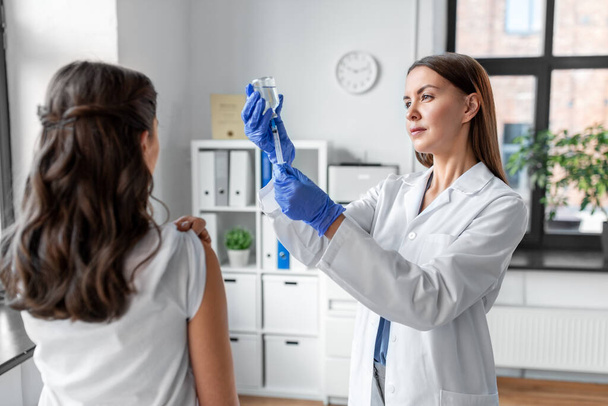 здоровье, медицина и пандемическая концепция - улыбающаяся женщина врач или медсестра в защитных медицинских перчатках со шприцем вакцинации пациента в больнице - Фото, изображение