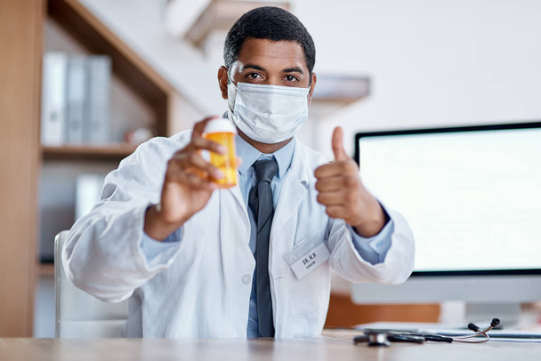 Trustworthy doctor selling good covid medicine or bottle of pills, approving successful medication in hospital. Male healthcare or medical professional wearing mask, showing thumbs up hand gesture - Valokuva, kuva
