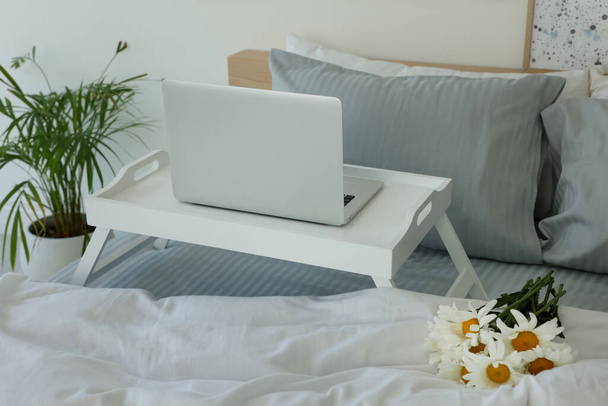White tray table with laptop and bouquet of beautiful daisies on bed indoors - Zdjęcie, obraz