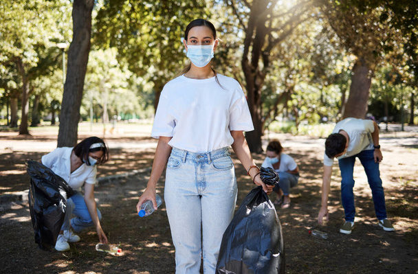 Covid, face mask and volunteer worker cleaning park, doing community service and helping pick up trash and plastic bottles. Support team of activists recycling, working together to end pollution. - Foto, Imagen