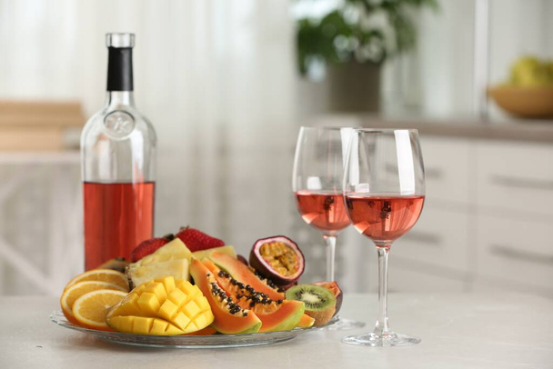 屋内の白いテーブルの上においしいエキゾチックな果物とワイン - 写真・画像