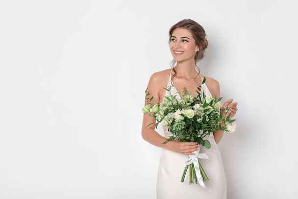 Young bride wearing wedding dress with beautiful bouquet on light background. Space for text - Φωτογραφία, εικόνα