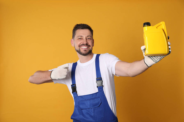 Man pointing at yellow container of motor oil on orange background - Zdjęcie, obraz
