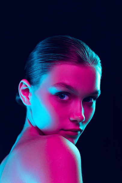 Fashion, style. Young beautiful girl with well-kept skin and without makeup isolated over dark background in neon light. Concept of natural beauty, art, emotions, cosmetics and youth - Foto, Imagen