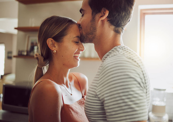 Affectionate, loving and romantic couple in a happy relationship together in the kitchen at home. Man and woman sharing a moment of happiness, romance and bonding with each other in love - Фото, изображение