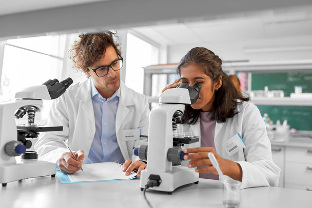 science research, work and people concept - international team of scientists with microscopes working in laboratory - Photo, Image