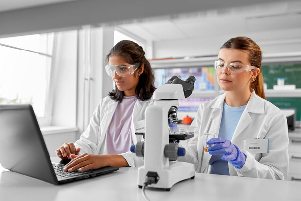 science research, work and people concept - international female scientists with microscope and laptop computer working in laboratory - Fotó, kép