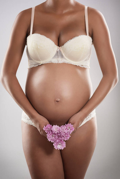 Her pregnancy is blooming beautifully. Studio shot of an unrecognizable pregnant woman holding flowers against a gray background - Foto, imagen