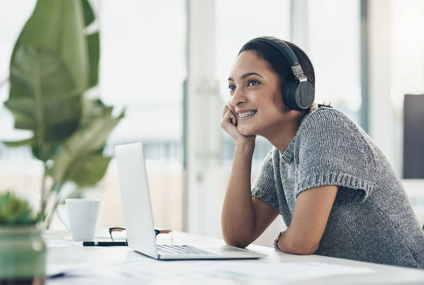 Happy, smiling business woman day dreaming of success at her office desk in a modern office. Female office worker enjoying a podcast or songs during a break in a corporate company over copy space - Foto, Imagen
