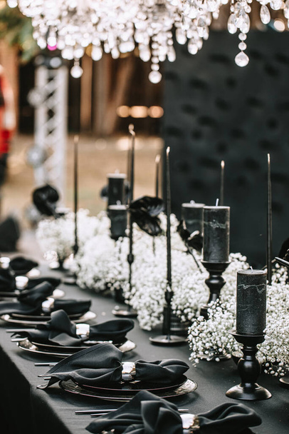 Serving and decorating a banquet table in black with white flowers and black candles at an outdoor party. - Fotografie, Obrázek