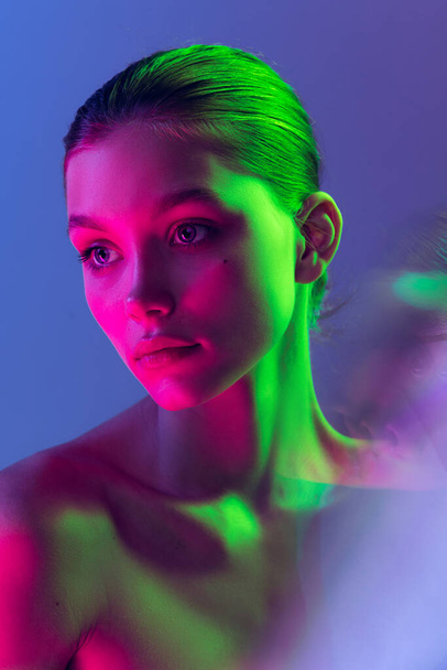 Serious and thoughtful. Attractive young, beautiful girl with well-kept skin isolated on blue background in neon light. Art, fashion, style, facial expression, eco products and health - Фото, изображение