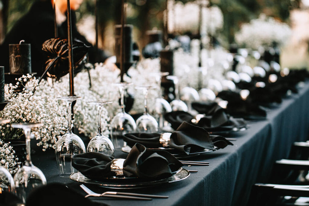 Serving and decorating a banquet table in black with white flowers and black candles at an outdoor party. - Foto, imagen