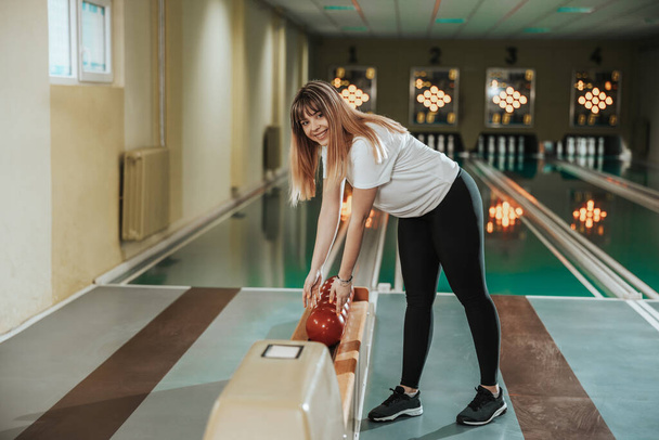 Shot of a cute young woman holding bowling ball in the bowling club. - 写真・画像