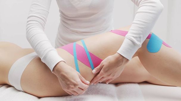 Therapist is applying kinesio tape to beautiful female body. Physiotherapy, kinesiology and recovery treatment. - Fotó, kép