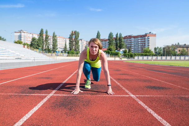 A young woman in the starting position for running on a sports track. Sportswoman at the start. - Foto, imagen