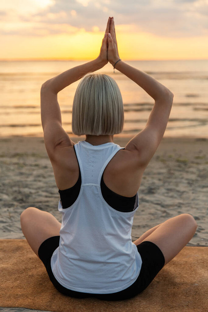 yoga, mindfulness and meditation concept - woman meditating in lotus pose on beach over sunset - Φωτογραφία, εικόνα