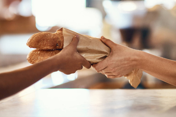 Customer buying bread from bakery, purchasing baked goods and shopping for food at a shop. Hands of female client and employee giving service, taking product and helping with item at grocery store. - Foto, imagen