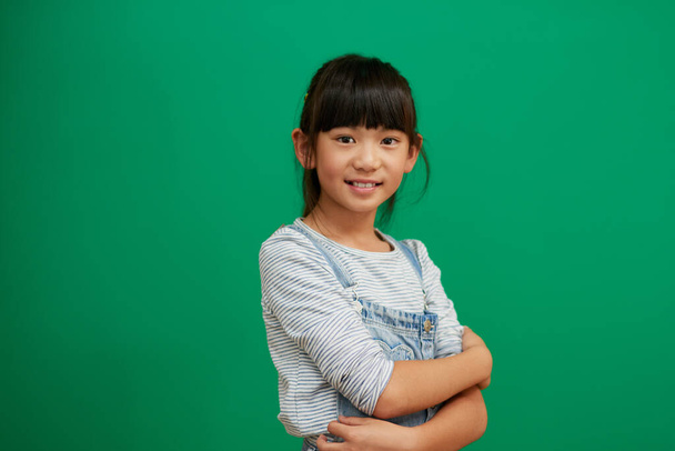 Its great being a kid. Studio portrait of confident little girl standing with her arms folded against a green background - Foto, imagen