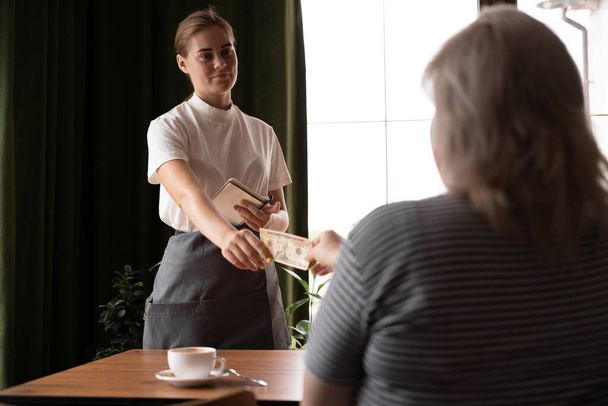 Female client pays in cash in a cafe, woman gives a dollar tip to a waitress, copy space - Foto, Bild