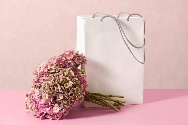 White shopping bag with beautiful bouquet on a pink background - Photo, Image