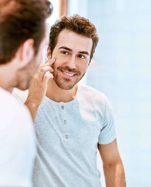 Hes loving the great results his skin regime is giving. a handsome young man checking his face at home - Zdjęcie, obraz