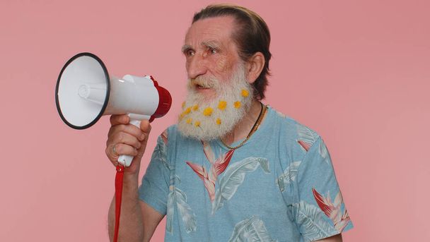 Happy bearded senior man talking with megaphone, proclaiming news, loudly announcing sale advertisement, warning using loudspeaker to shout speech. Elderly mature grandfather on pink studio background - Photo, image